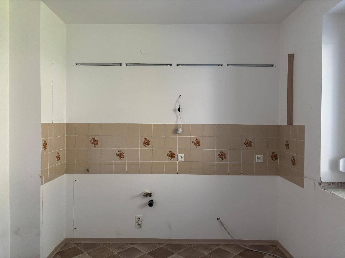 Küchenwand mit beigen Fliesen und floralen Mustern, bereit für die Installation einer neuen Küche.