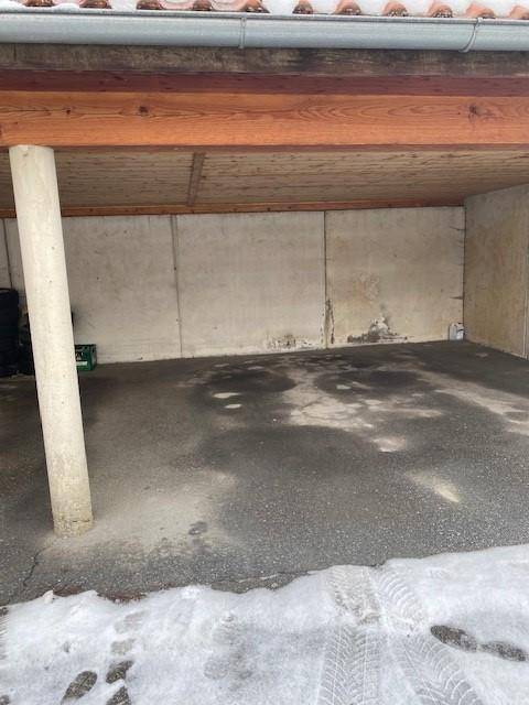 Überdachter Stellplatz im Freien mit Betonwänden und Asphaltboden, teilweise mit Schnee bedeckt.