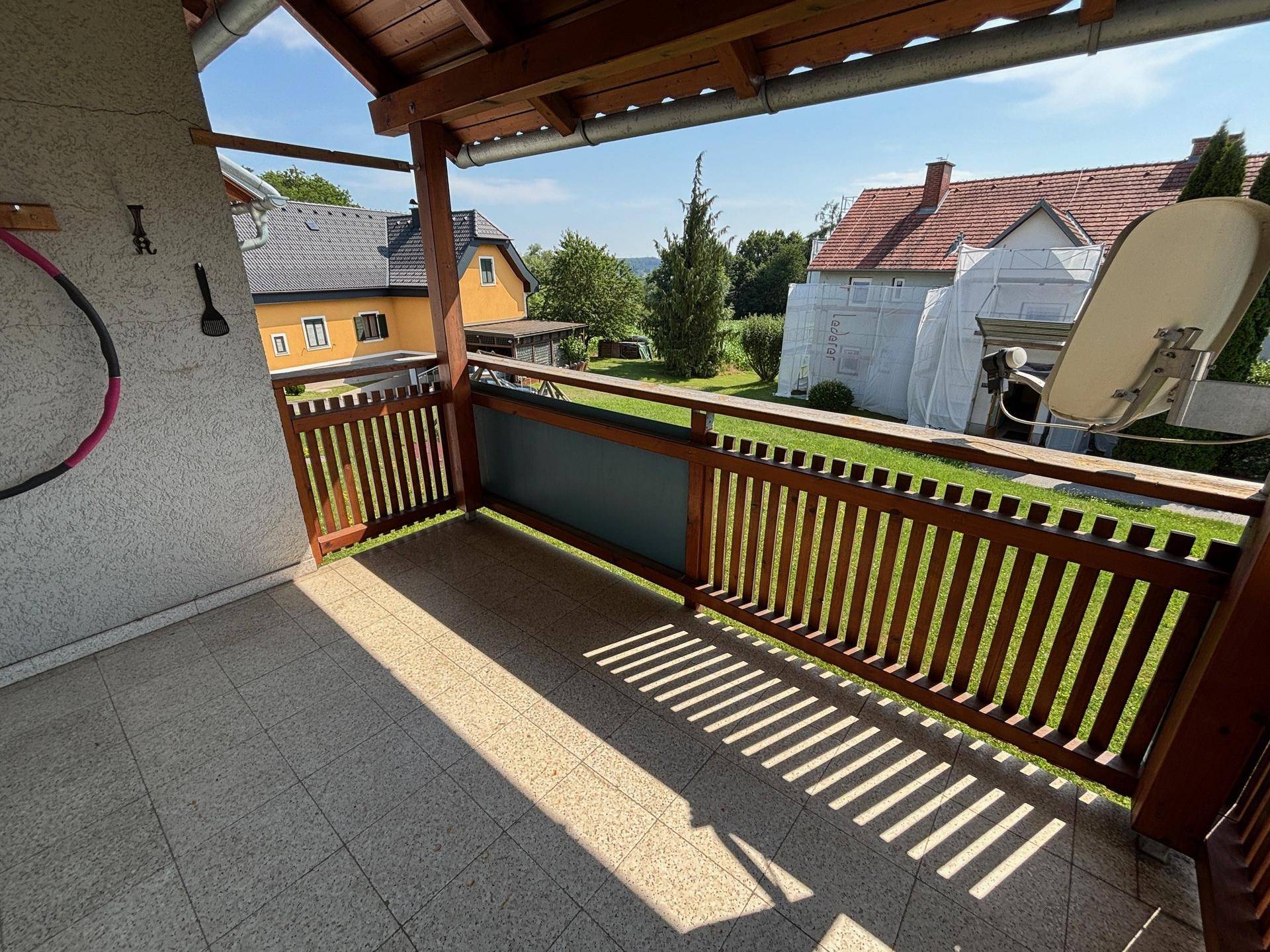 Sonniger Balkon mit Fliesenboden, Holzgeländer und Blick auf die umliegende Wohngegend.
