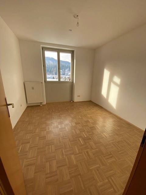 Leeres Schlafzimmer mit Parkettboden und Fenster, das viel Tageslicht und Bergblick bietet.