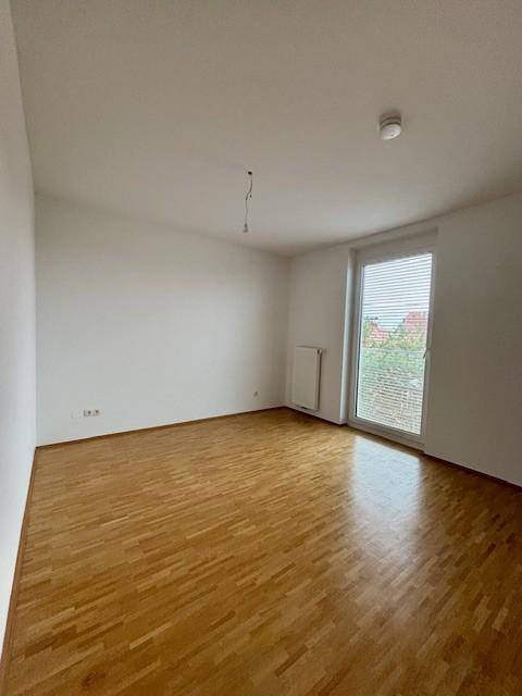 Helles Zimmer mit Parkettboden und Fenster mit Jalousien für optimalen Lichteinfall.
