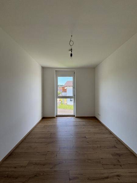 Helles, leeres Zimmer mit Holzboden und einem hohen Fenster, ideal als Schlaf- oder Arbeitszimmer.