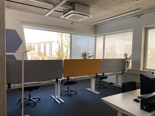 Büroarbeitsplätze mit Blick auf die Umgebung durch große Fenster, ausgestattet mit Sichtschutzpaneelen.