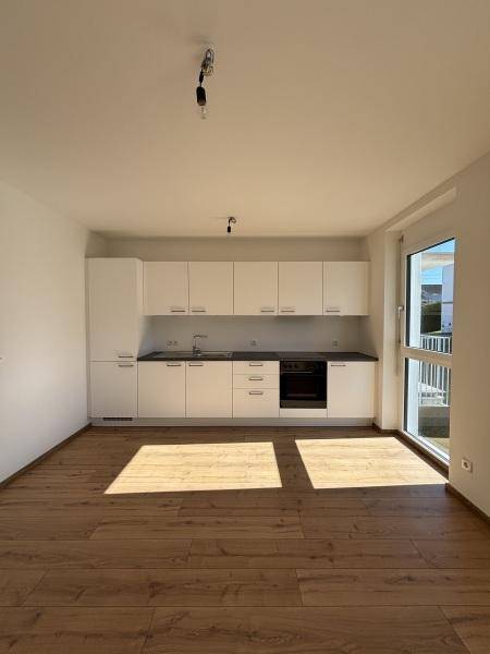 Helle, offene Küche mit weißen Schränken, Einbauherd und Holzplankenboden, mit Balkonzugang.