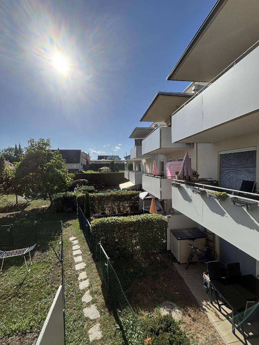 Sonniger Balkon mit Blick auf den grünen Garten und die umliegende Wohngegend.
