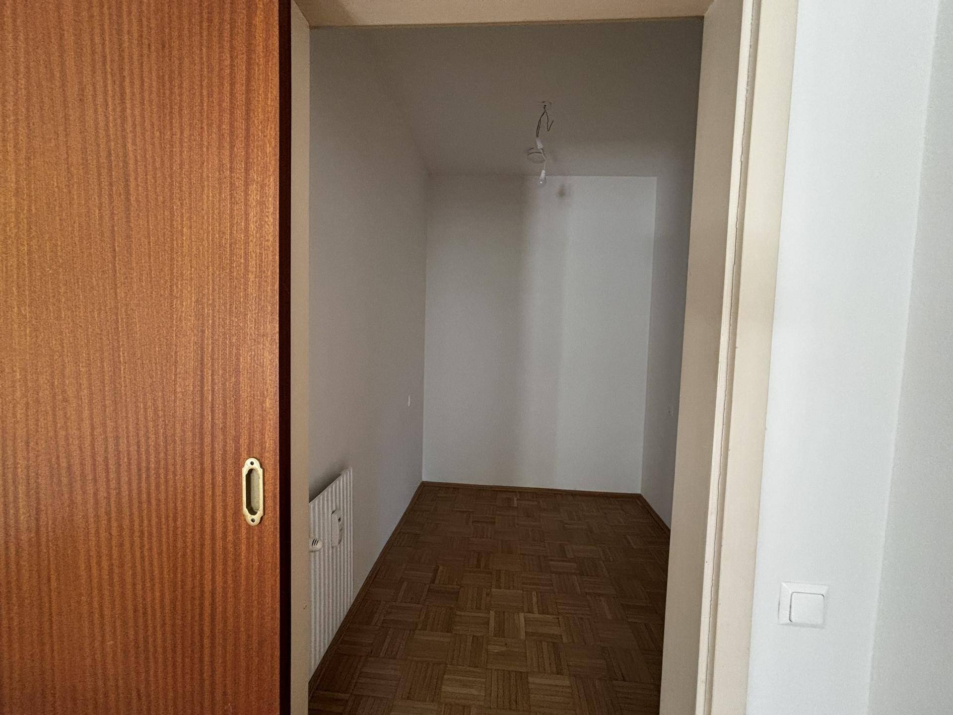 Kleiner, leerer Raum mit Parkettboden und einer Holztür, ideal als Abstellraum oder begehbarer Schrank.