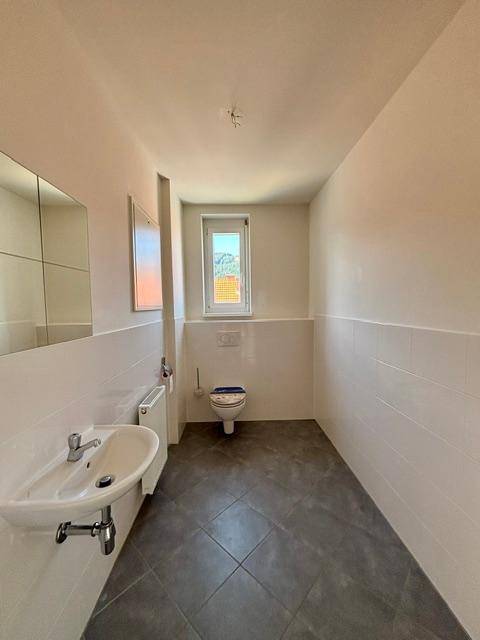 Helles Gäste-WC mit dunklem Fliesenboden, wandhängendem WC und einem Fenster.
