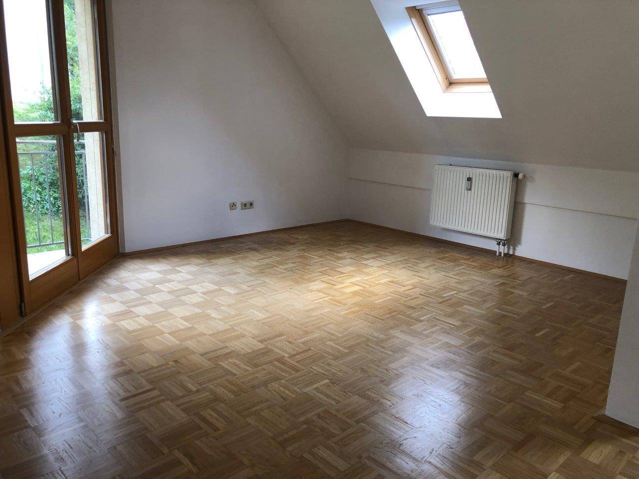 Heller Dachbodenraum mit Parkettboden, Dachfenster und Zugang zu einem kleinen Balkon.