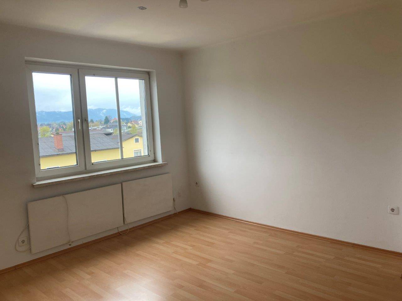 Leerer Raum mit Laminatboden, großem Fenster und weitem Blick auf die umliegende Landschaft und Berge.