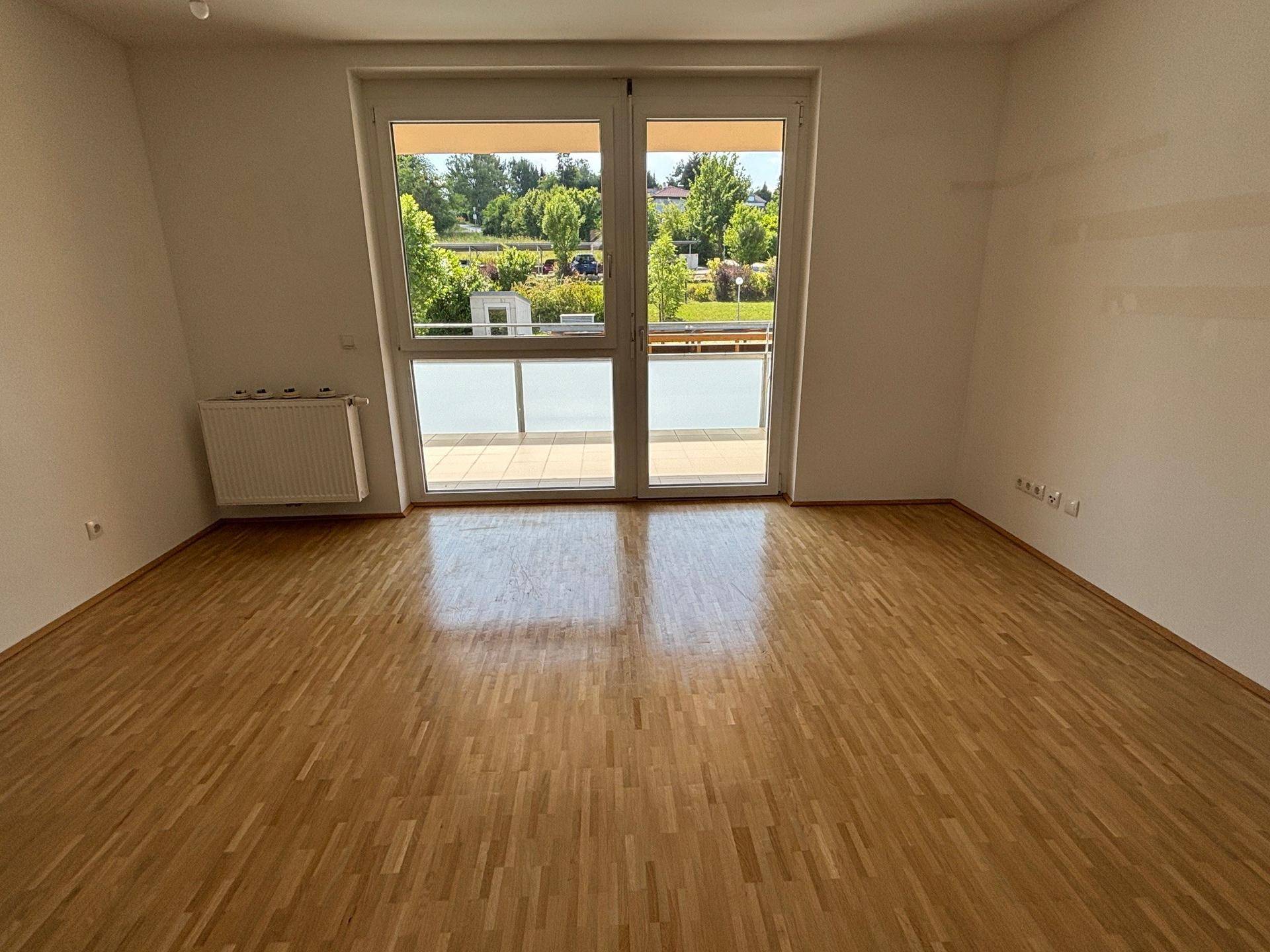 Großes Zimmer mit Holzboden, breiten Fenstern und Balkonzugang, bietet viel Tageslicht.