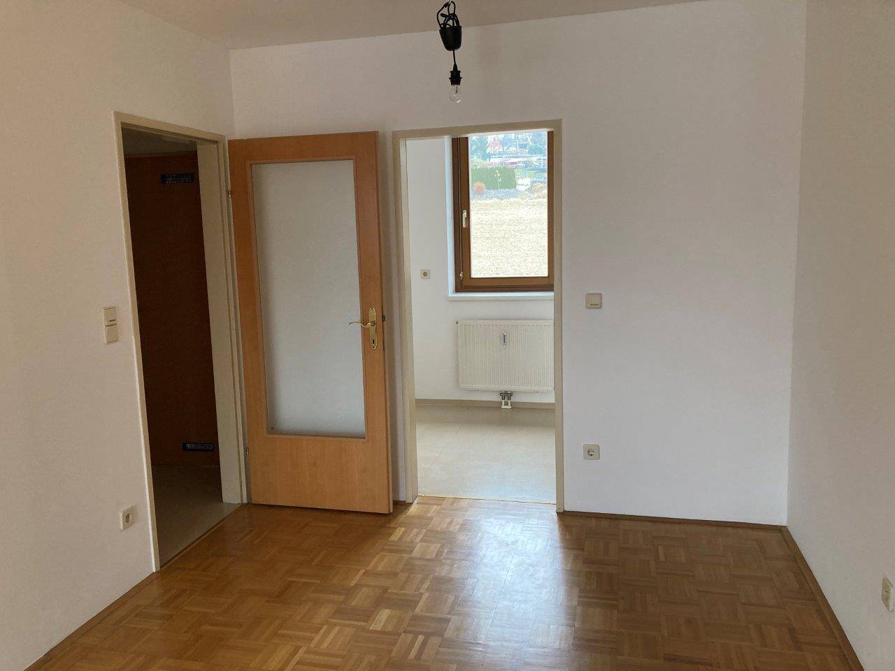 Leerer Raum mit Parkettboden und Tür zu einem weiteren Zimmer, gut beleuchtet.