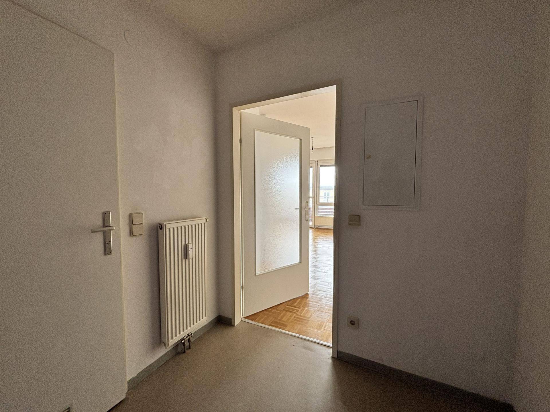 Heller Flur mit Heizkörper und einer Tür, die in einen weiteren Raum führt.