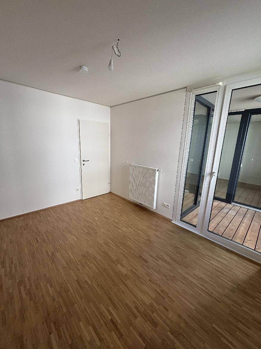 Helles Zimmer mit Holzparkettboden und großem Glaszugang zu einem Außenbereich.