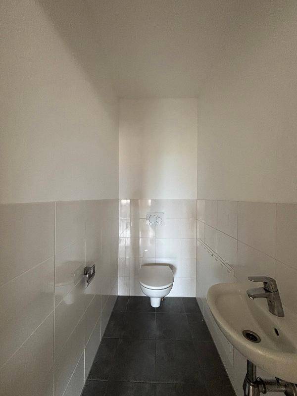 Kleines Gäste-WC mit wandhängendem WC, Waschbecken und dunklen Bodenfliesen.