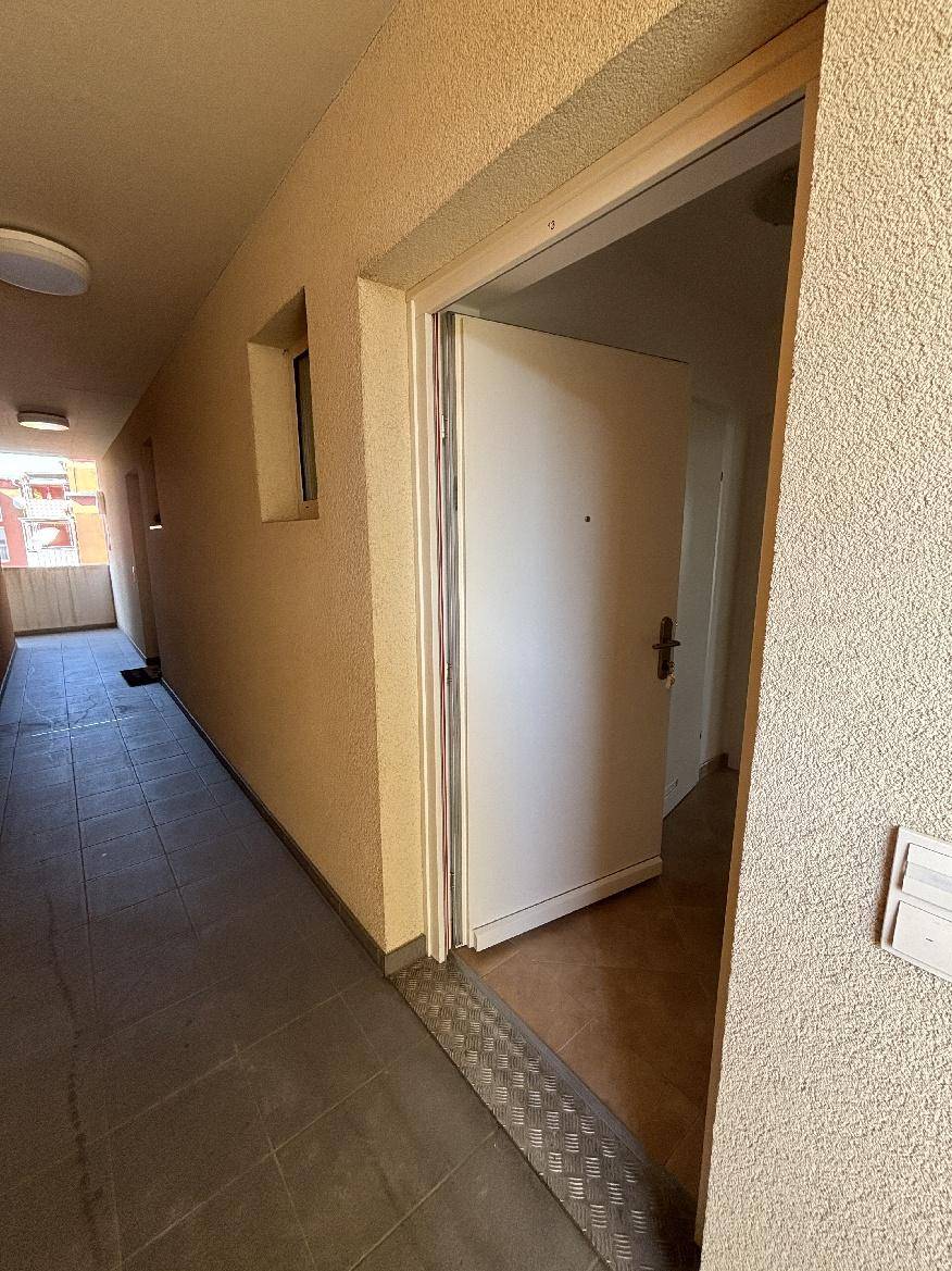 Eingangsbereich eines Mehrfamilienhauses mit gefliestem Boden und offener Wohnungstür.