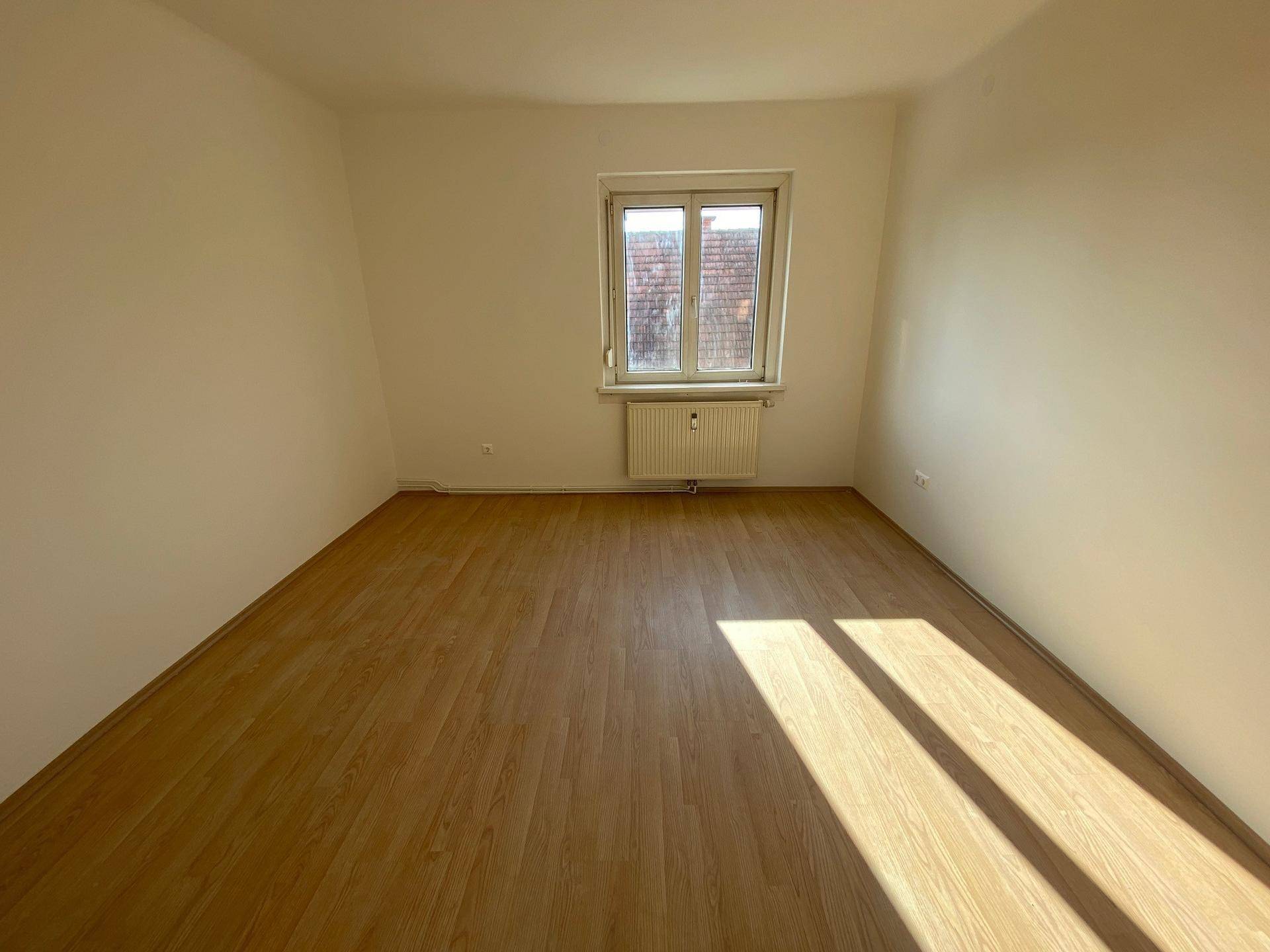 Geräumiger, heller Raum mit Laminatboden und Fenster mit Blick ins Grüne.