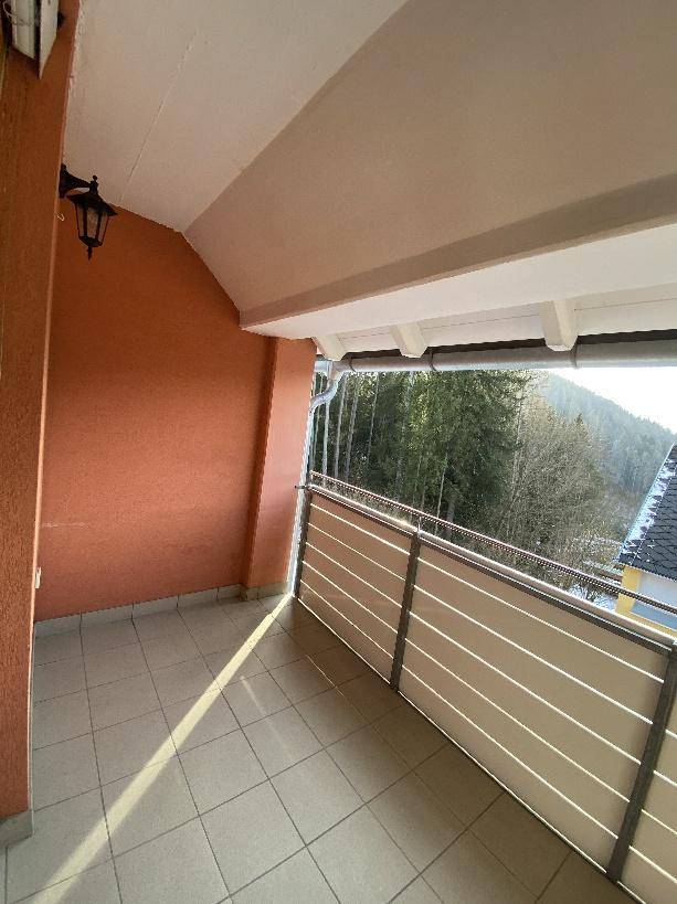 Überdachter Balkon mit Fliesenboden und Blick auf die bewaldeten Hügel.