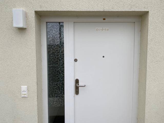 Weiße Eingangstür mit seitlichem Glaspanel und Klingelanlage an einer modernen Fassade.