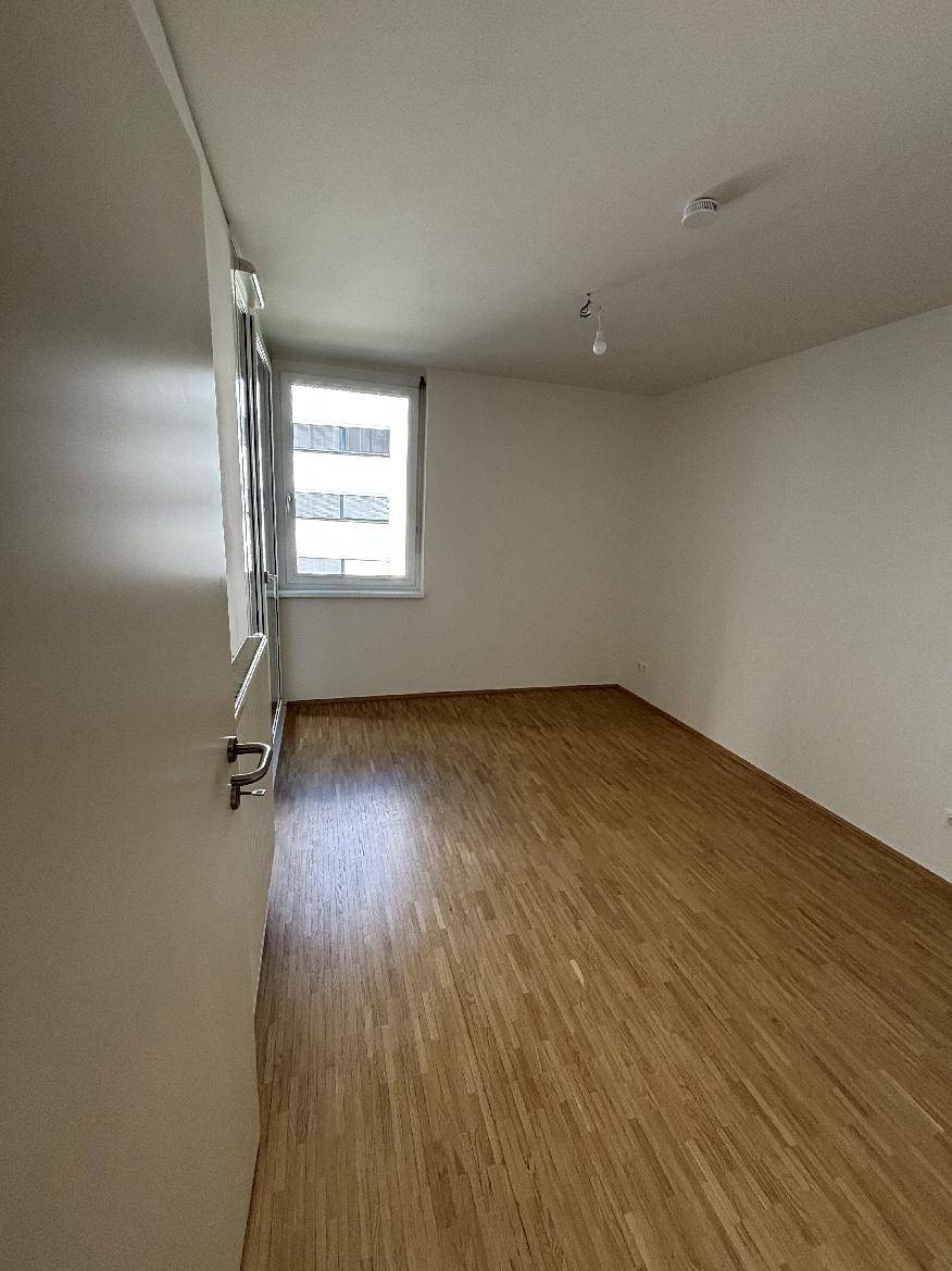 Leeres Zimmer mit hellem Holzparkettboden und einem Fenster, ideal als Schlafzimmer.
