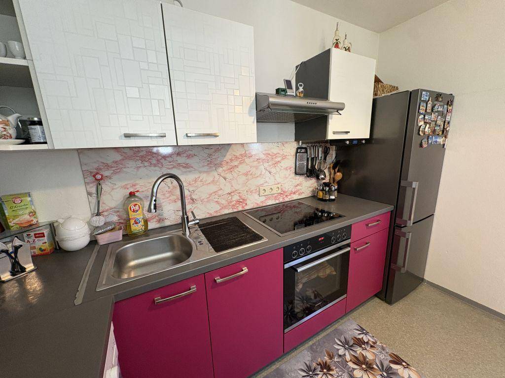 Moderne Küche mit pinkfarbenen Unterschränken, weißen Oberschränken und integrierten Geräten.