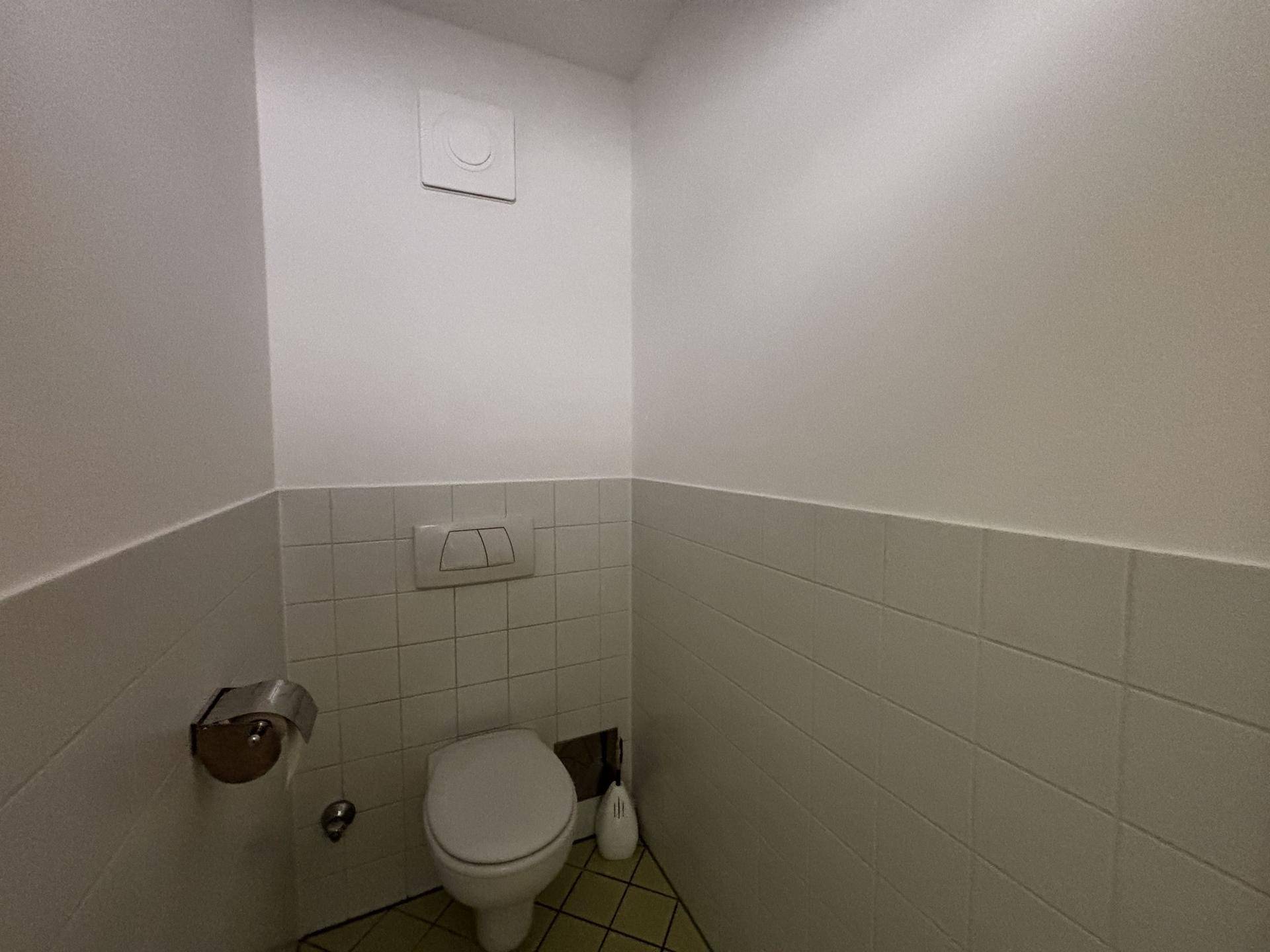 Separates WC mit wandhängender Toilette und weißen Fliesen an den Wänden.