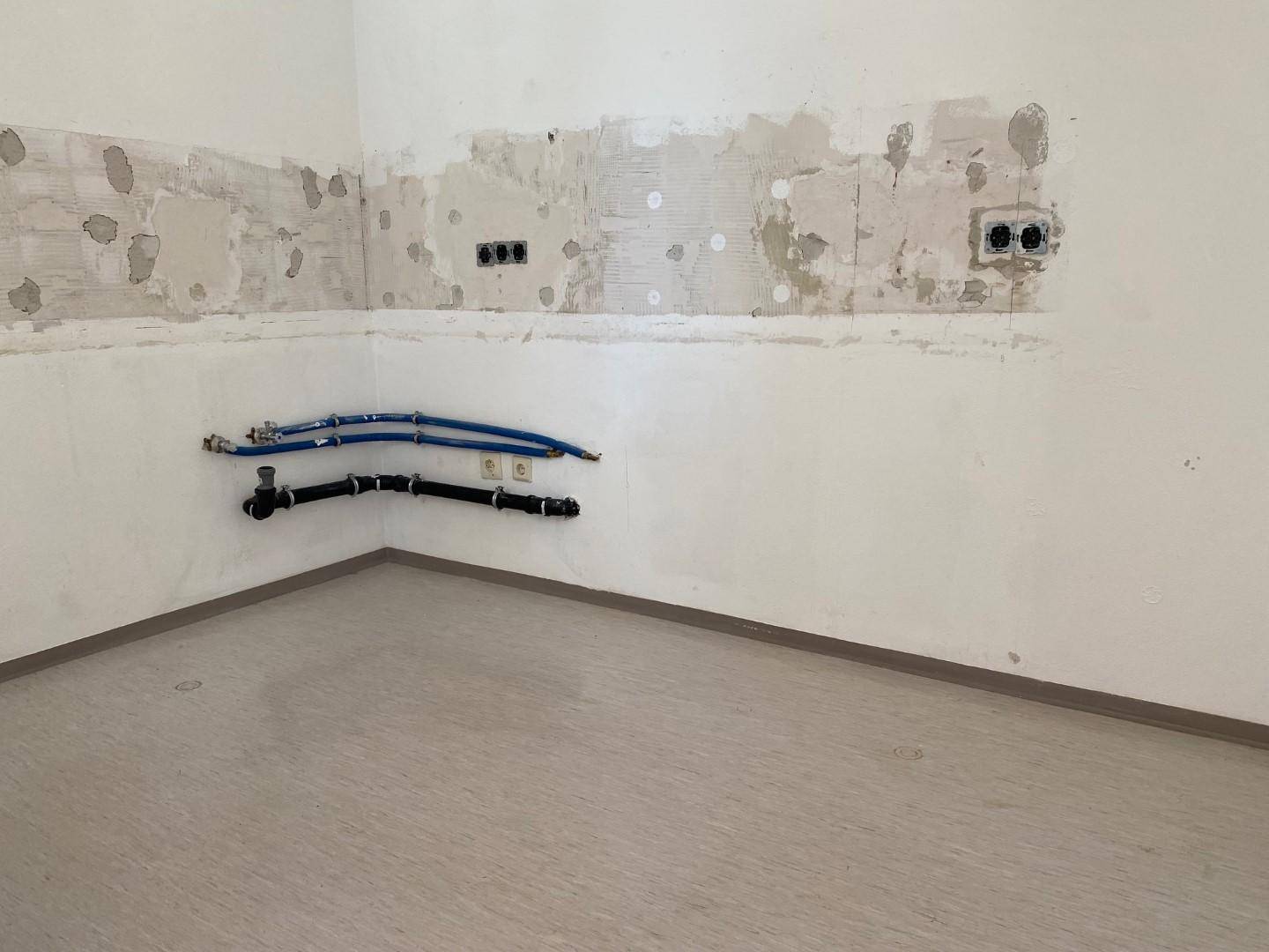 Leerer Küchenraum mit vorbereiteten Anschlüssen für die Installation einer neuen Küche.