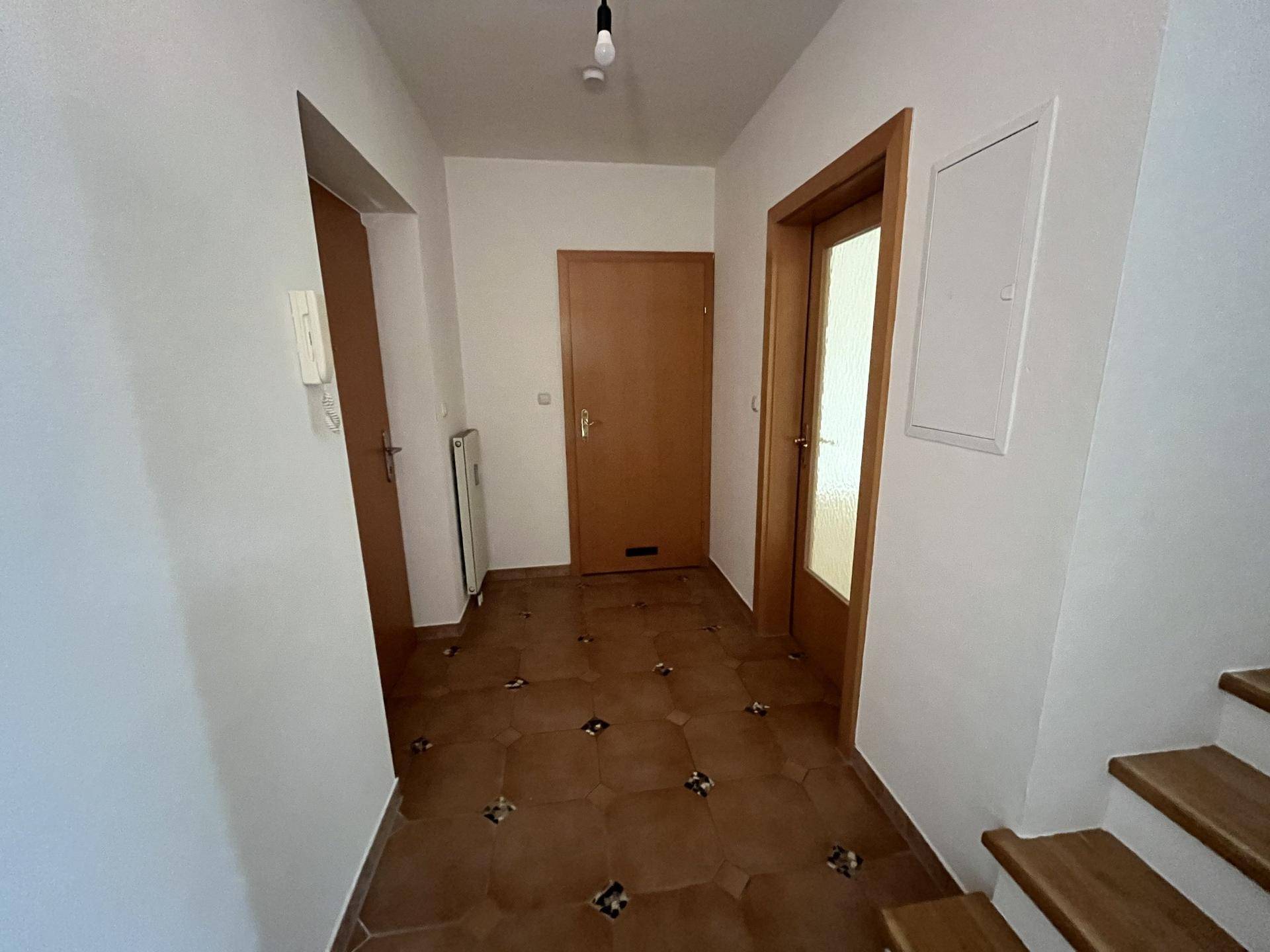 Eingangsbereich mit Terrakotta-Fliesenboden, Holztüren und Zugang zur Treppe.