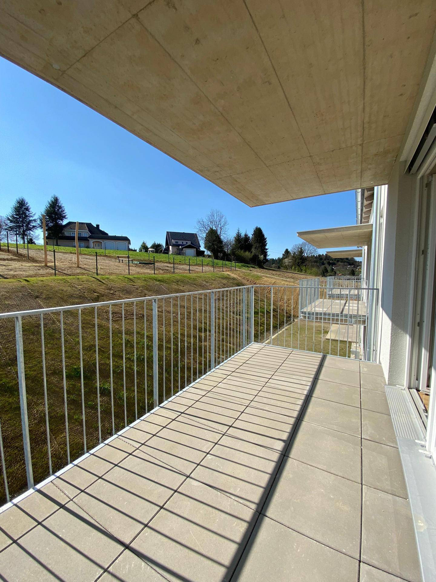 Geräumiger Balkon mit Fliesenboden und Blick auf die grüne Landschaft und entfernte Häuser.