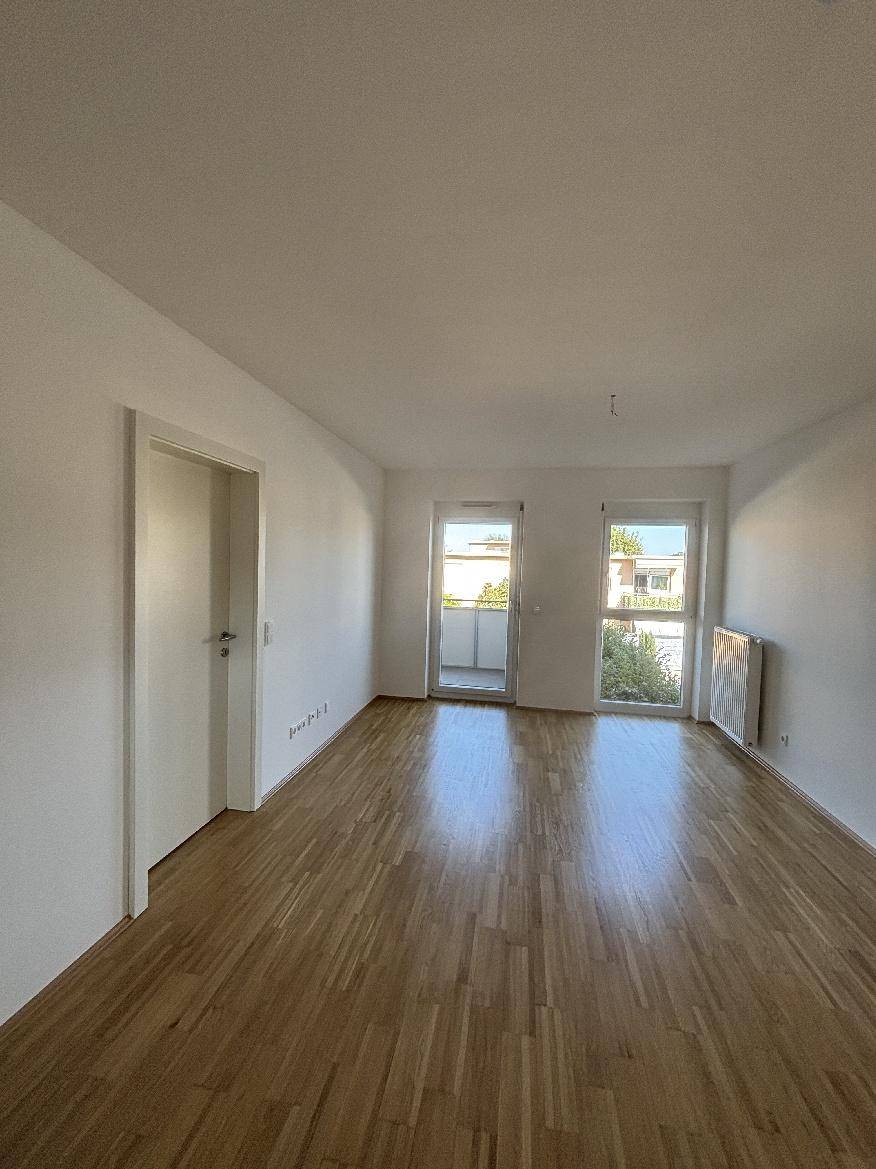 Geräumiges Wohnzimmer mit Holzparkettboden und direktem Zugang zum Balkon.