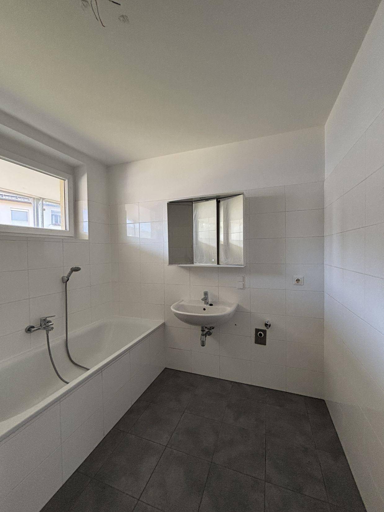 Helles Badezimmer mit Badewanne, Waschbecken und Spiegelschrank, ausgestattet mit weißen Fliesen.