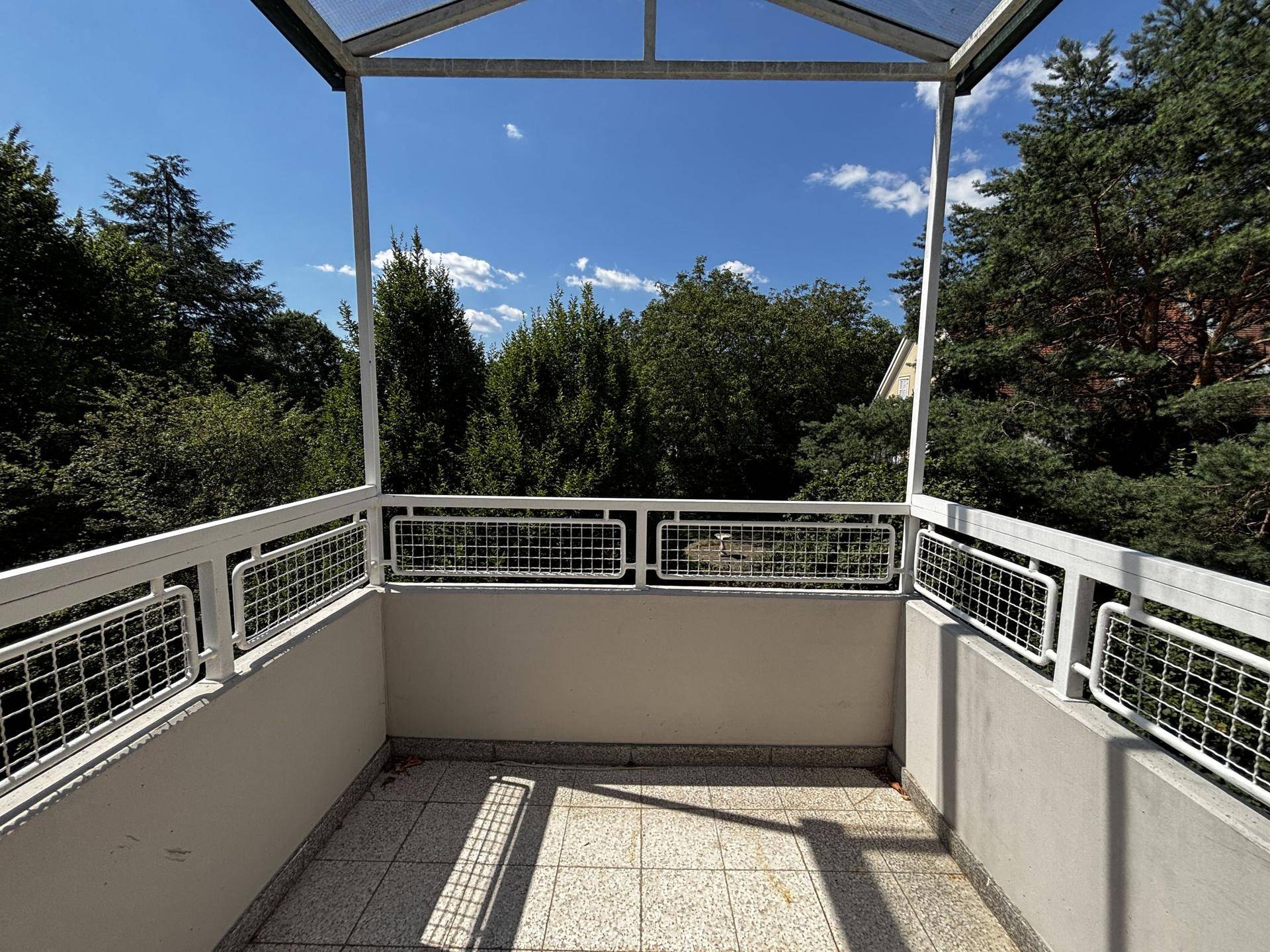 Geräumiger Balkon mit Glasdach, Fliesenboden und einem schönen Blick ins Grüne.
