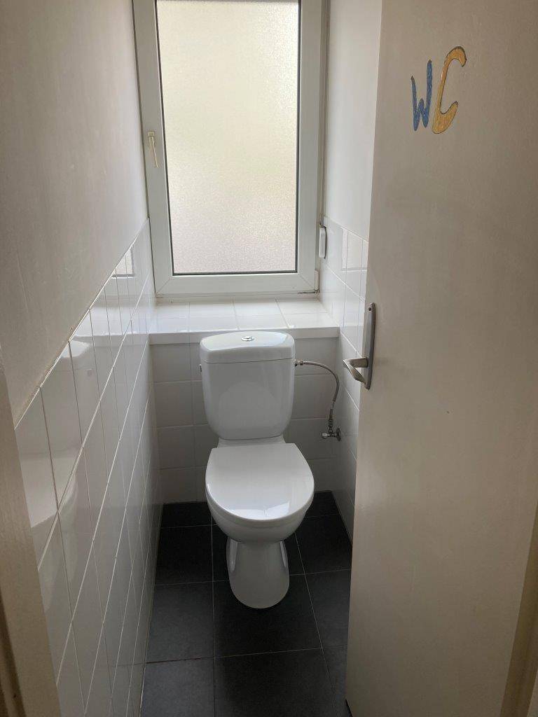 Separates WC mit Fenster, Toilette und weißen Wandfliesen.