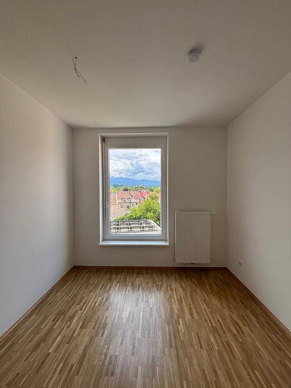 Freundliches Zimmer mit Parkettboden und großem Fenster, bietet einen schönen Ausblick ins Grüne.