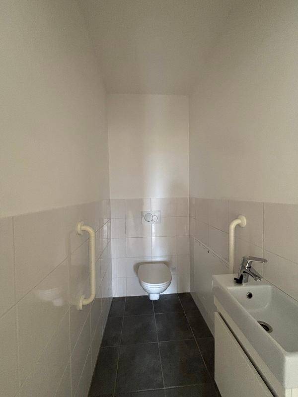 Kleines Gäste-WC mit Wand-WC, Handwaschbecken und Haltegriffen für Barrierefreiheit.