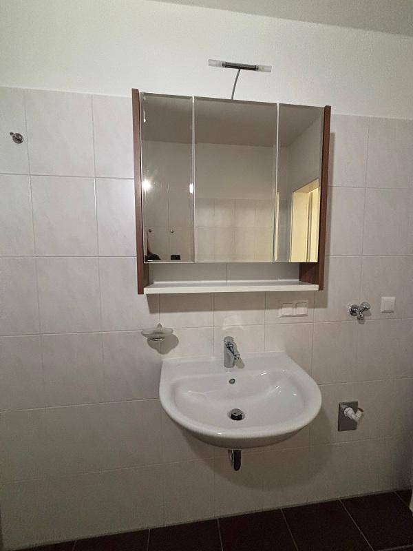 Badezimmer mit Waschbecken, Spiegelschrank und weißen Wandfliesen.