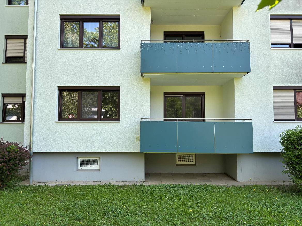 Fassadendetail des Gebäudes mit Balkonen und Fenstern, umgeben von Grünflächen.