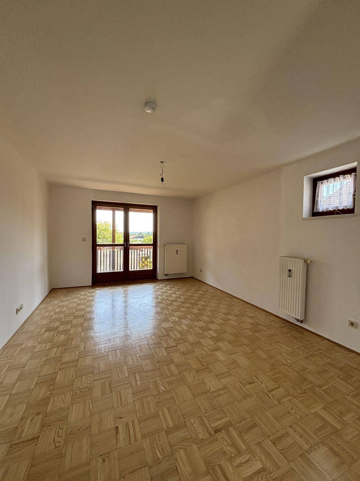 Geräumiges Wohnzimmer mit Parkettboden, Heizkörpern und Zugang zu einem Balkon.