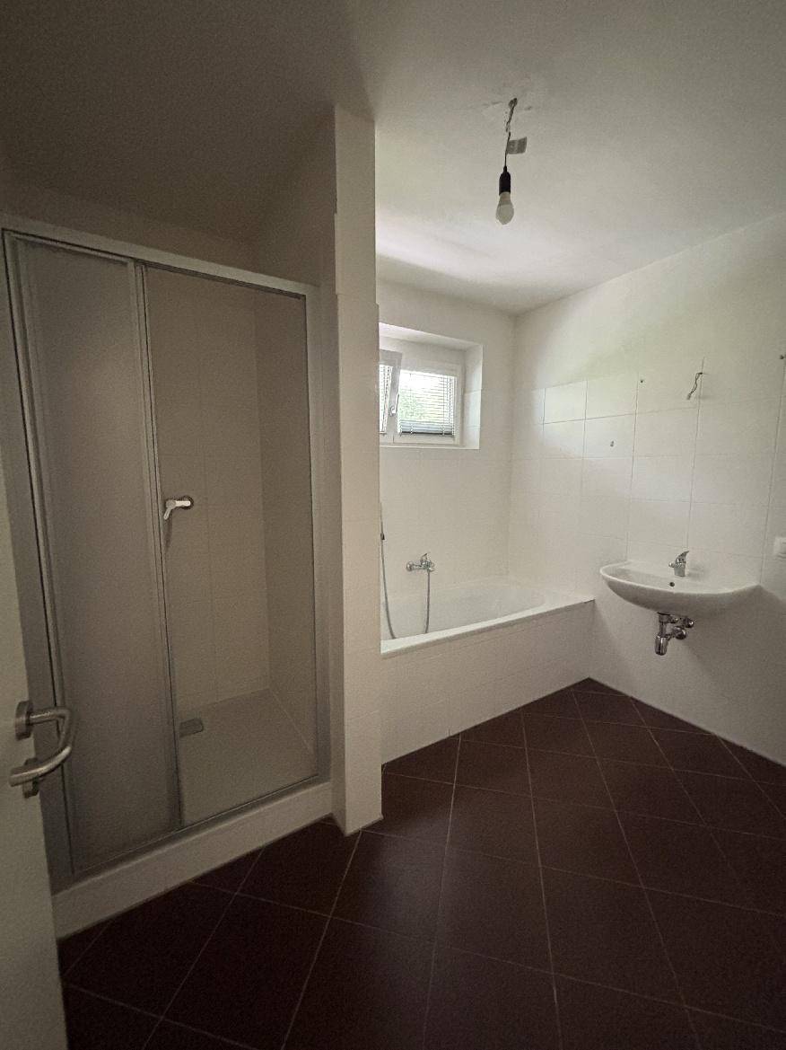 Funktionales Badezimmer mit Duschbereich, Badewanne und Waschbecken, hell gefliest.