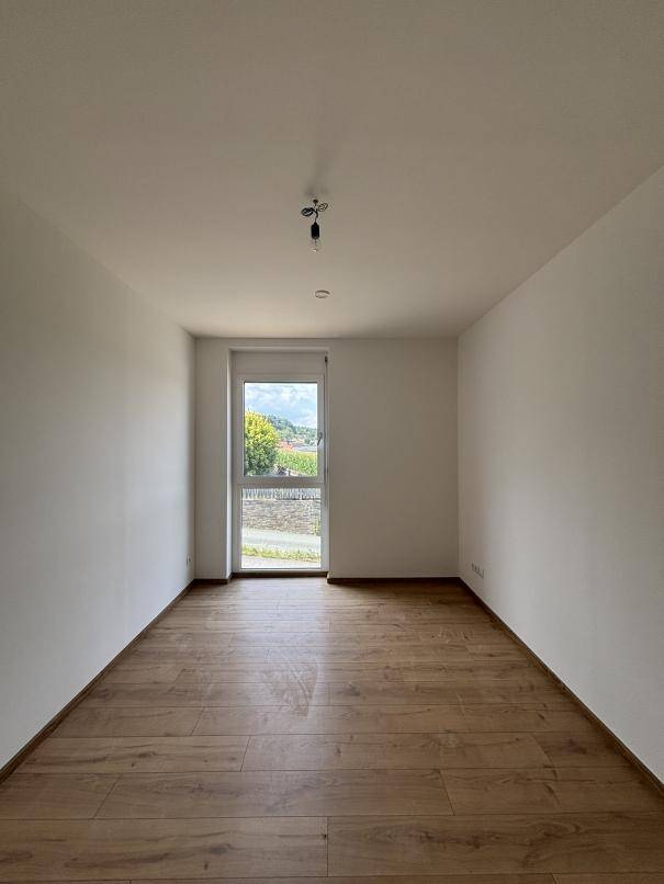 Geräumiges Zimmer mit Holzboden und großem Fenster, bietet viel Tageslicht und eine angenehme Atmosphäre.
