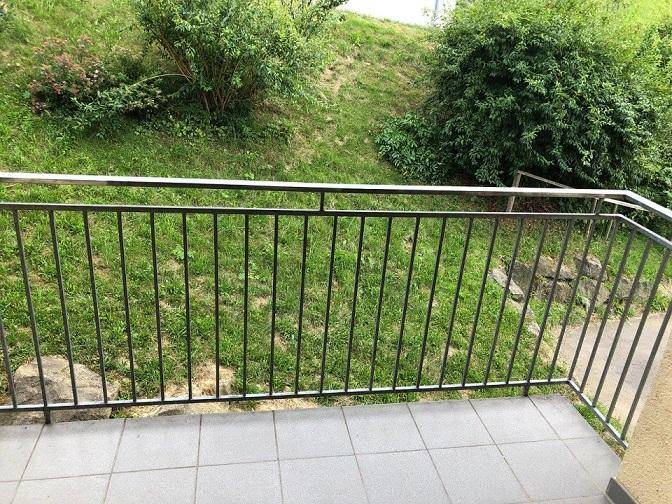 Kleiner Balkon mit Fliesenboden und Blick ins Grüne, umgeben von Büschen.