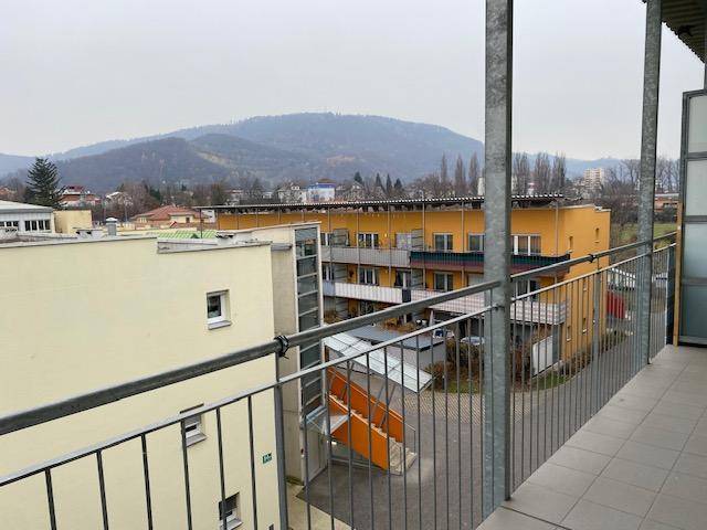 Weitblick vom Balkon über Wohngebäude und eine hügelige Landschaft im Hintergrund.