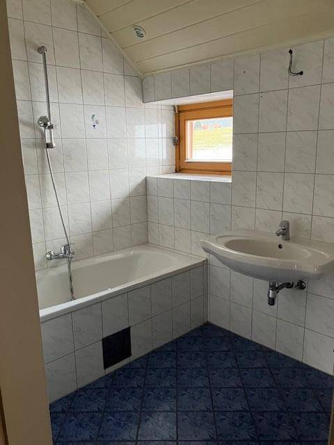 Gefliestes Badezimmer mit Badewanne, Waschbecken und Fenster.
