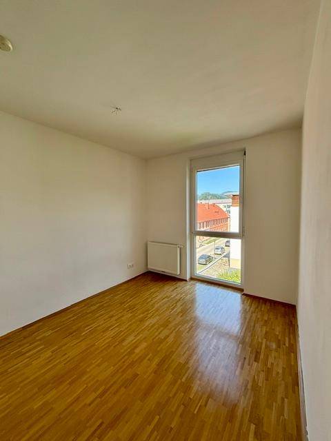 Geräumiges Zimmer mit hellem Parkettboden und Fenster, das einen Blick auf die Straße bietet.