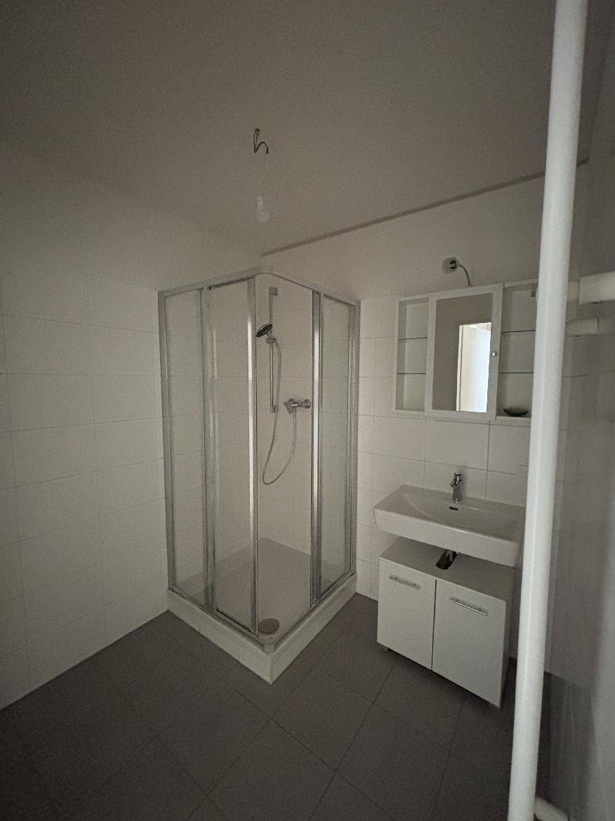 Modernes Badezimmer mit Duschkabine, Einzelwaschbecken und grauen Bodenfliesen.