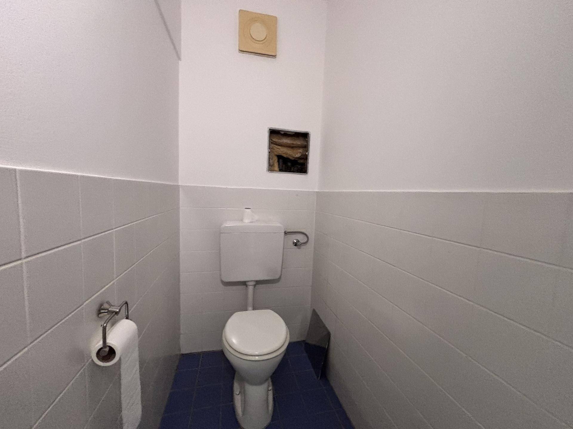 Separate Toilette mit WC, Fliesen und einem Lüftungssystem an der Wand.