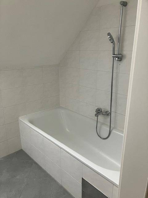 Modernes Badezimmer mit Badewanne und weißen Fliesen unter einer Dachschräge.