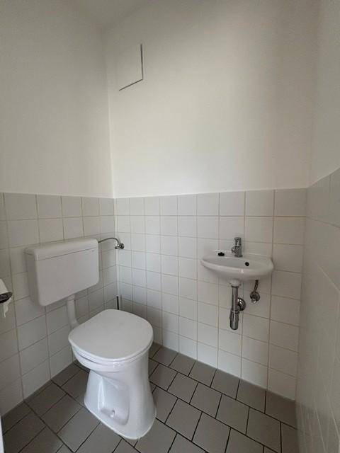 Kleines Gäste-WC mit weißer Toilette, Waschbecken und hellen Fliesen an Wänden und Boden.