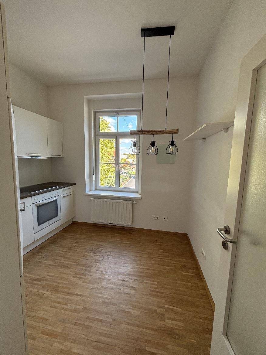Helle Küche mit Einbauküche, Parkettboden und einem Fenster mit Blick ins Grüne.