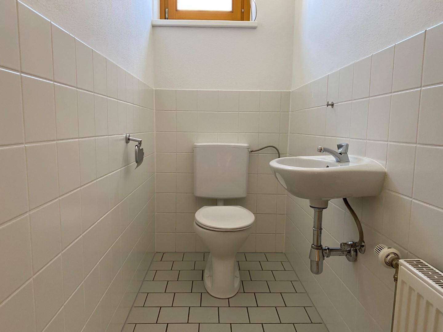 Gäste-WC mit Toilette, Waschbecken und weißen Fliesen an Wänden und Boden.