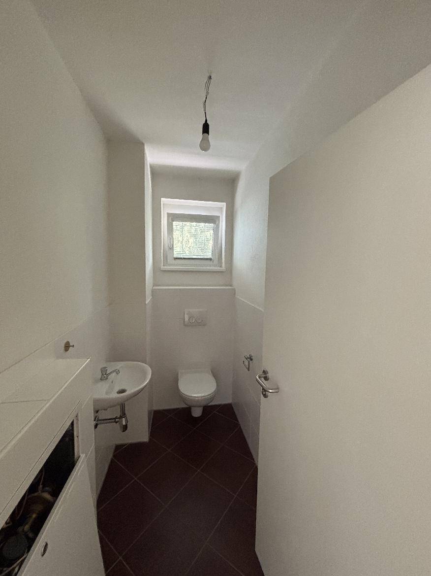 Kleines Gäste-WC mit Toilette, Waschbecken und Fenster für natürliche Belüftung.